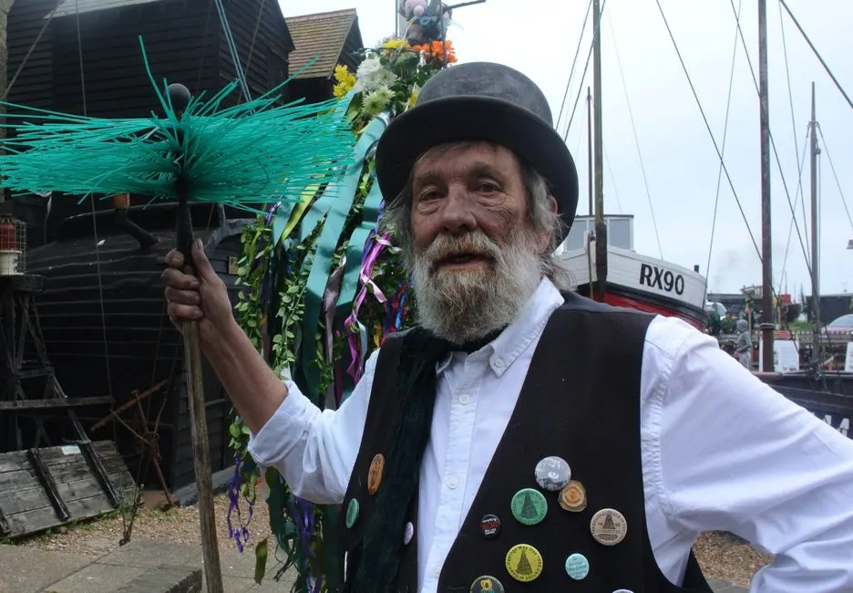 Elderly man in traditional costume participating in outdoor festival with vibrant decorations and boats.
