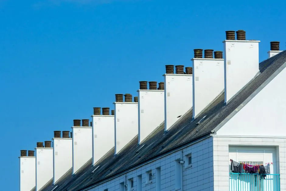 Row of chimneys on modern residential buildings under a clear blue sky. Urban architecture with rooftops.